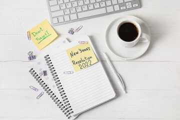 Cup of coffee, computer keyboard, stationery, sticky notes with text NEW YEAR'S RESOLUTION 2022 and DON'T FORGET on white wooden background