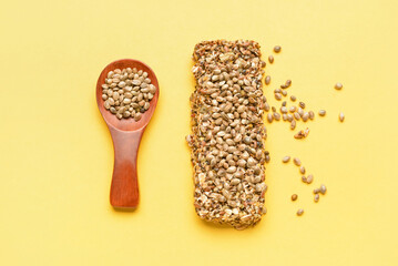 Protein bar with hemp seeds and spoon on yellow background