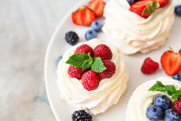 Stand with tasty Pavlova cakes and fresh berries on grunge background, closeup