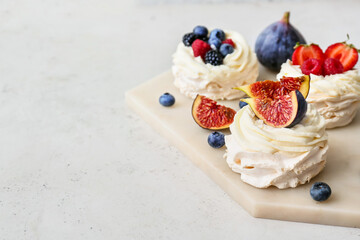 Board of tasty Pavlova cakes with berries on light background, closeup