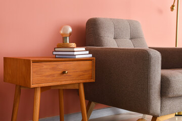 Wooden table with lamp, books and armchair near pink wall