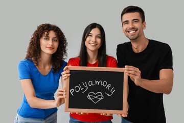 Man and two women holding chalkboard with word POLYAMORY on grey background - obrazy, fototapety, plakaty