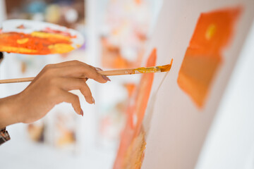 female artists hand holding a paint brush with color palette painting in studio