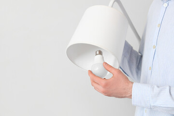 Woman changing light bulb in standard lamp near light wall, closeup