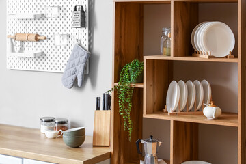 Wooden shelving unit with dishware, coffee maker and houseplant near light wall in kitchen