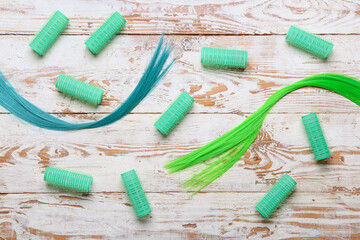 Green hair strands with curlers on light wooden background