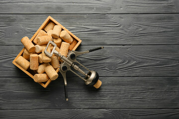 Box with wine corks and opener on black wooden background