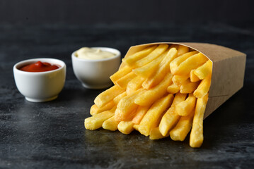 Paper box with tasty french fries on black background