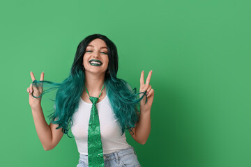 Young woman in wig showing victory gesture on green background. St. Patrick's Day celebration
