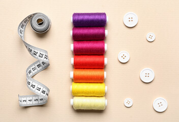 Sewing threads, measuring tape and buttons on beige background