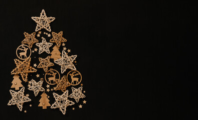 Christmas tree made of stars and wooden toys on a black background. Stars from rattan and toys from wood.Copy space. Flatlay.
