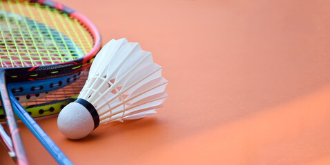Cream white badminton shuttlecock and racket on red floor in indoor badminton court, copy space, soft and selective focus on shuttlecocks.