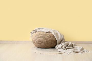 Beige pouf with blanket on rug near yellow wall