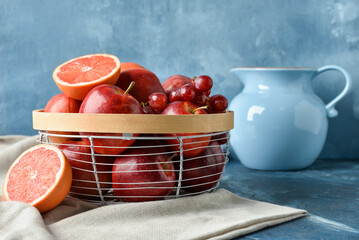 Basket with fresh juicy fruits and jug on color background