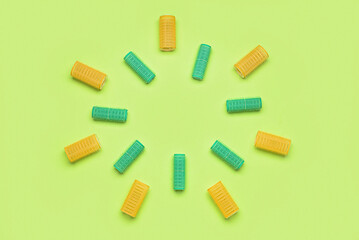 Frame made of different hair curlers on green background