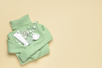 Folded sweater, cosmetic products and winter decor on color background