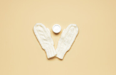 Knitted mittens and jar with cream on color background