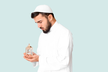 Praying young Muslim man with fanous lamp on light background