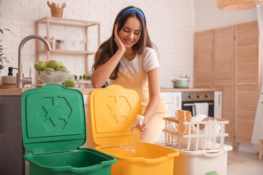 Young woman putting plastic bottle into bin in kitchen