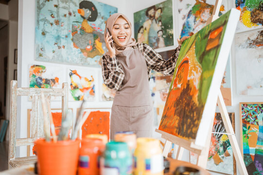 muslim asian female artist painting on canvas and talking to phone