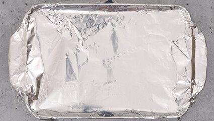 Baking dish covered with aluminum foil close up on the table, flat lay. Spinach lasagna recipe.