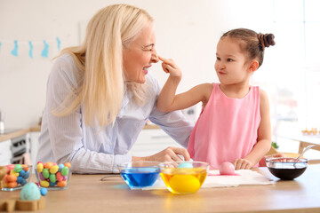 Little girl having fun with her grandmother while painting Easter eggs at home