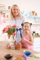 Happy little girl and her grandmother with Easter eggs and bouquet of flowers at home