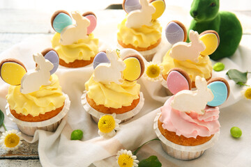 Tasty Easter cupcakes and flowers on light wooden background, closeup