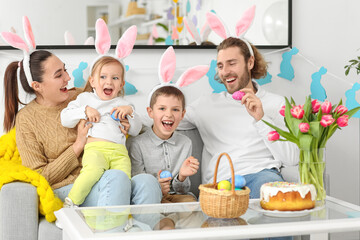 Happy family in bunny ears with Easter eggs sitting on sofa at home