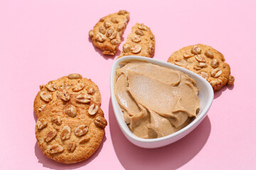 Tasty peanut cookies and bowl with butter on pink background