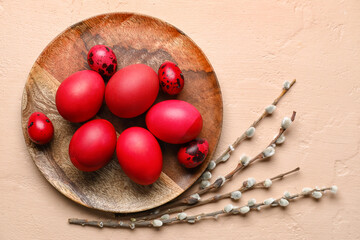 Plate with beautiful Easter eggs and pussy willow branches on color background