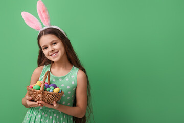 Cute little girl with bunny ears and Easter basket on green background