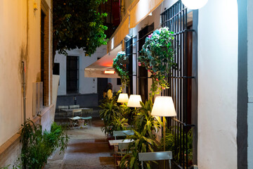 A narrow side street with tables from a cafe in the Barrio Santa Cruz district of Seville, Spain.