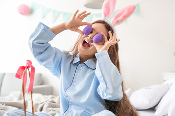 Cute little girl with bunny ears and Easter eggs in bedroom