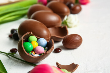 Broken chocolate Easter egg with different candies on light background, closeup