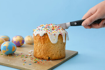 Woman cutting delicious Easter cake on blue background