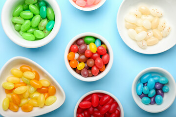 Bowls with different jelly beans on blue background