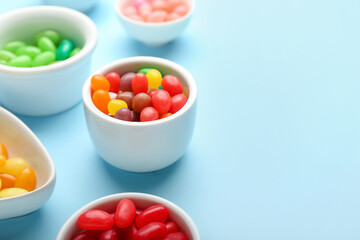Bowls with different jelly beans on blue background, closeup