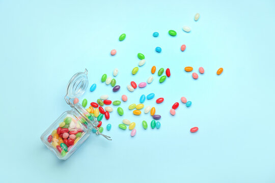 Glass jar with different jelly beans on blue background
