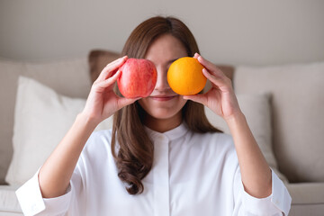 A beautiful young woman holding and covering eyes with an orange and a red apple