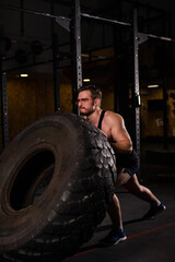 Plakat Caucasian man pushing a car tire in the gym. 