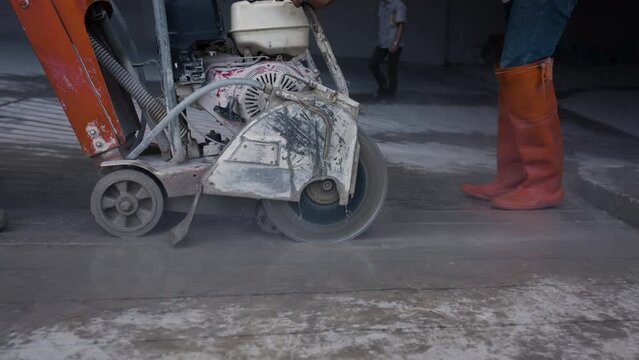 4K, Construction workers use machines to cut concrete roads in a parking lot. And there were fragments of mortar on the concrete floor scattered all over the machinery and shoes.