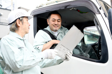 会話をするトラックに乗る作業服を着たミドル男性達