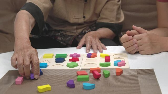 Caregiver and senior woman playing wooden shape puzzles game for dementia prevention.
