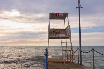 An empty rescue tower stands on a breakwater on the shore. Gray sunset, cloudy sky and stormy sea....