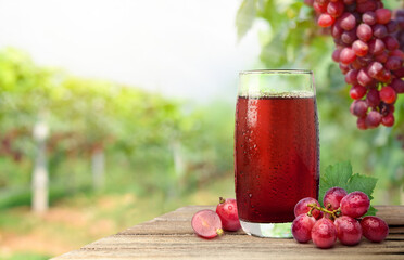 Cool red grape juice with grape plantation background.