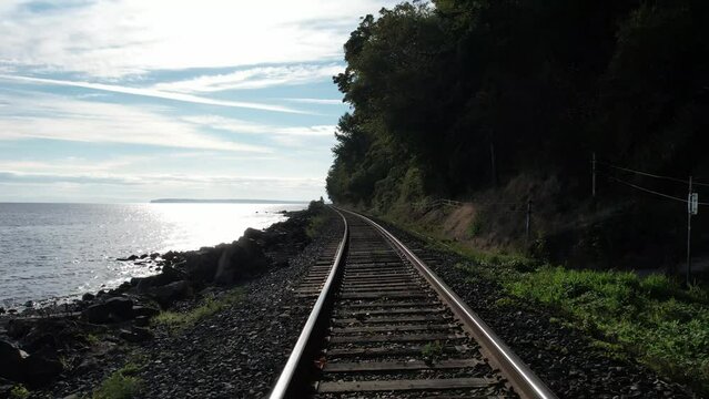 4k Drone footage of a locomotive eye view moving backward on the train tracks along the ocean coastline. Someplace in western Canada.