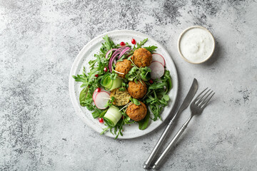 Falafel and fresh vegetables salad on a white ceramic plate on concrete background, top view. 