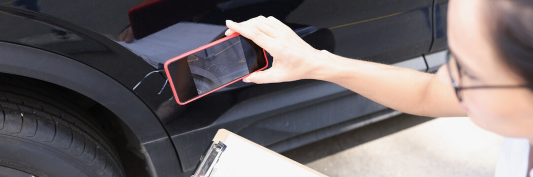 Insurance agent woman taking pictures on mobile phone of damaged car closeup