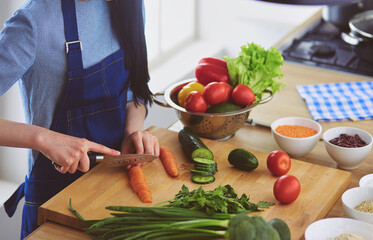 Young woman cutting vegetables in kitchen at home